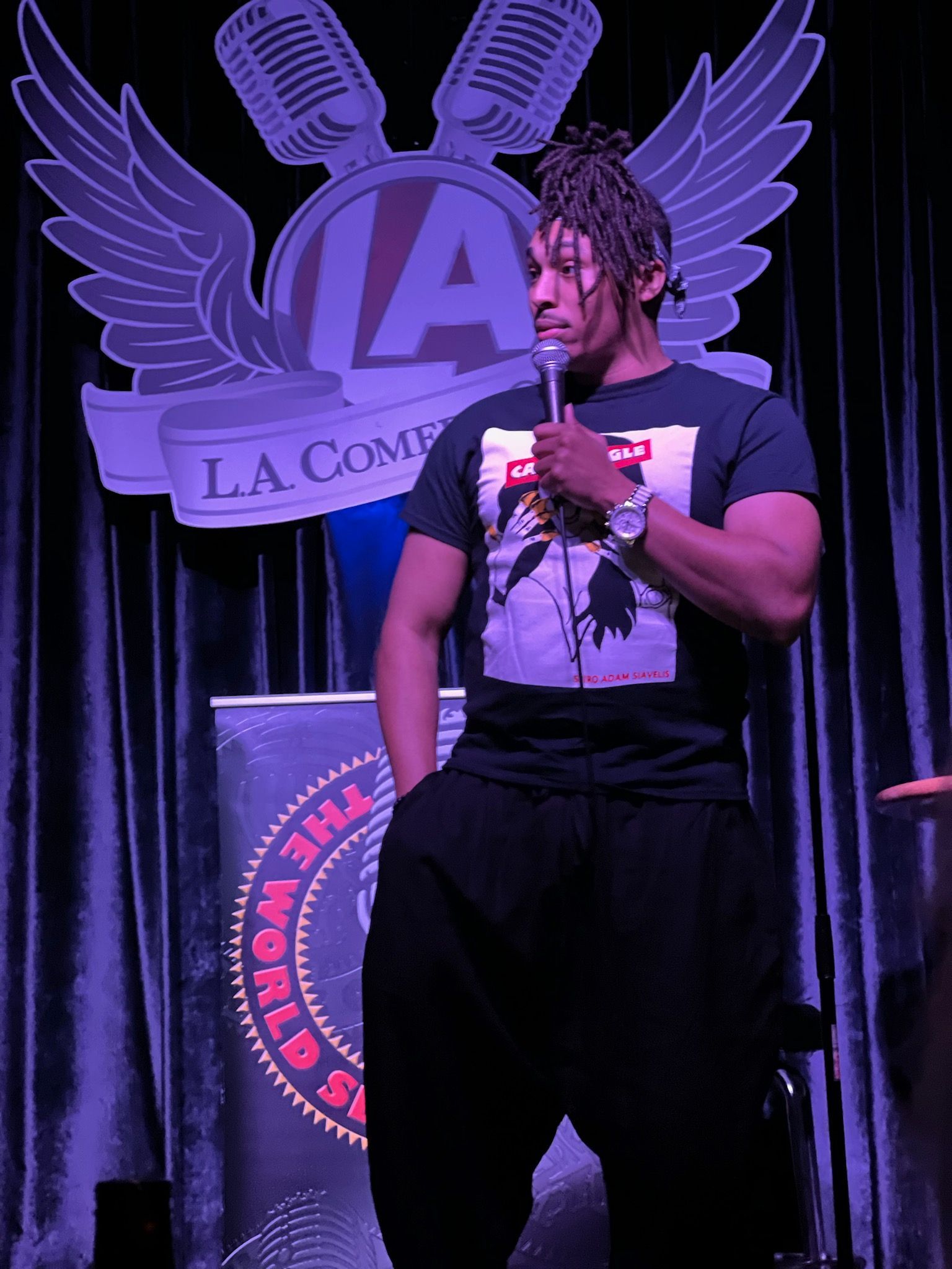 Jeremiah performing with a microphone on a purple-lit comedy stage